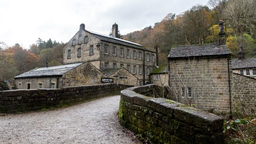 View across the bridge towards Gibson Mill on a late autumn day. The skies are grey and the leaves have turned, with trees in the background almost bare.